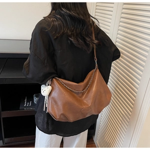 Detailed close-up of dark brown textured leather tote with a white bear charm and chain
