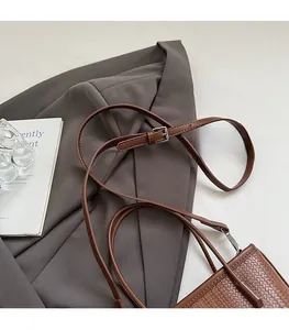 Detail showing the adjustable slim brown shoulder strap and woven texture of the bucket bag