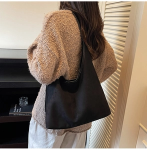 Gros plan d'un grand sac hobo noir mat avec surpiqûres verticales porté à l'épaule