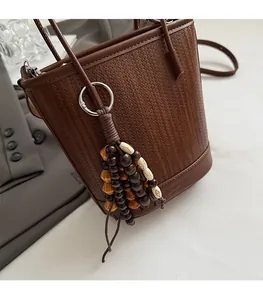 Detail of coffee woven bucket bag with bohemian wooden bead charm and crossbody strap