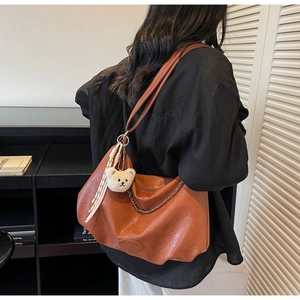 Caramel leather hobo bag with gold chain and plush bear charm on a model's shoulder