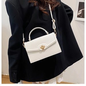 Detail of white litchi pattern leather bag with golden oval twist lock on black blazer