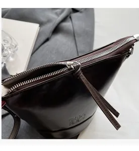 Close-up of the smooth silver zipper and leather puller on the dark brown bucket bag