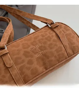 Close-up of caramel suede shoulder bag with silver metal rings and brand logo embossing