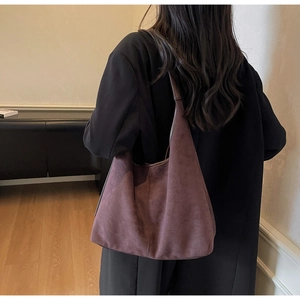 Détail du grand sac cabas hobo en daim bordeaux porté avec un manteau noir élégant