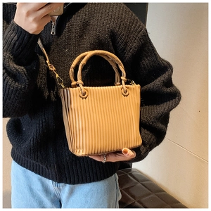 Detail showing the vertical pleated texture and cylindrical handles of this tan bucket bag