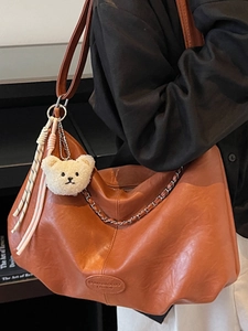 Brown leather slouchy hobo bag with gold chain and plush bear charm on shoulder