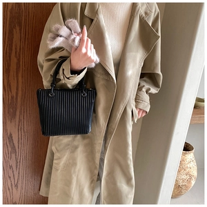 Detail of black pleated bucket bag featuring vertical texture and circular metal buckles