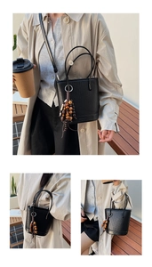 Detailed view of black woven bucket bag with wood bead tassel charm for casual look