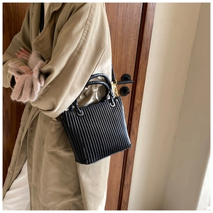 Detail of a chic black pleated bucket bag with gold hardware worn with a beige trench coat