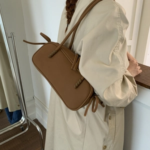 Detail shot of a brown matte leather Boston bag with decorative knots and thin strap