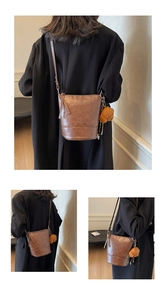 Detail view of a vintage brown bucket bag with embossed logo and cute teddy bear charm