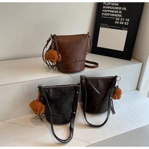 Detailed view of leather bucket bags in brown and black with plush poodle charms