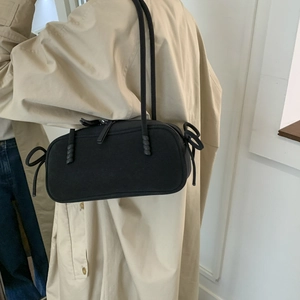 Detail of minimalist black frosted shoulder bag with side bow ties on beige trench coat