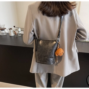 Detail of black vintage bucket bag with leather texture and cute brown plush teddy charm