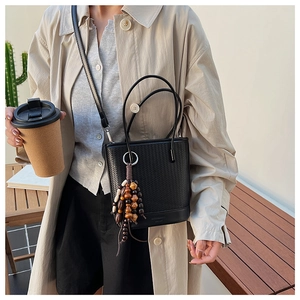 Detail of black woven bucket bag with vintage wooden beaded tassel and slim strap