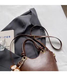 Detailaufnahme der braunen PU-Leder-Handtasche mit zylindrischen Griffen und Anhänger
