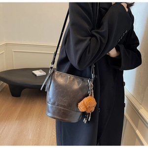 Detail of vintage brown leather bucket bag with embossed logo and cute teddy bear charm