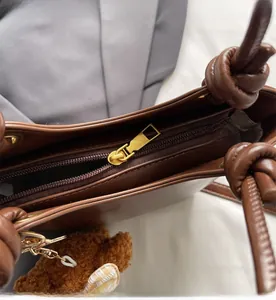 Detail einer braunen Ledertasche mit glattem Metallreißverschluss und Teddy-Anhänger