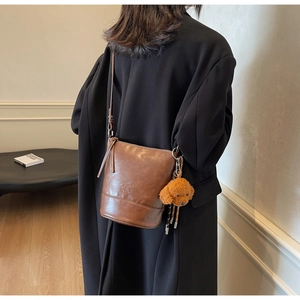 Detail view of deep brown leather bucket bag with a cute teddy bear plush charm