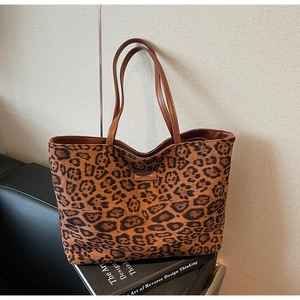Close-up of leopard print tote bag with brown leather handles and a centered logo patch