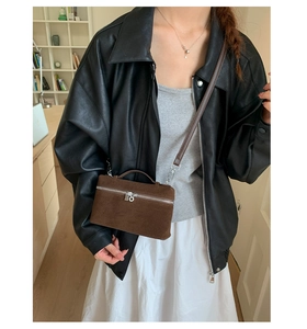 Braune Box-Tasche aus Wildleder an Model mit Lederjacke und weißem Kleid