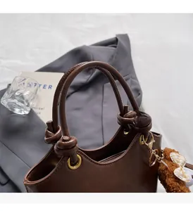 Detail einer dunkelbraunen Handtasche mit Knotengriffen und braunem Teddybär-Anhänger