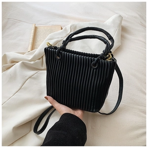 Detailed view of black pleated bucket bag with gold hardware on a minimalist background