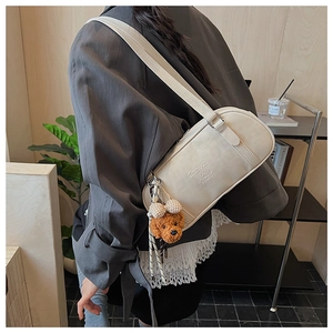 Detail of cream faux leather shoulder bag with plush teddy bear charm and brand logo