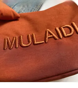 Macro detail of caramel fabric bag with MULAIDI brand embroidery and texture