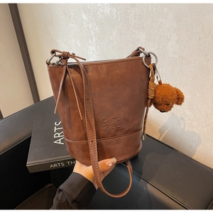 Detail of vintage brown bucket bag with plush bear charm and embossed logo on leather surface