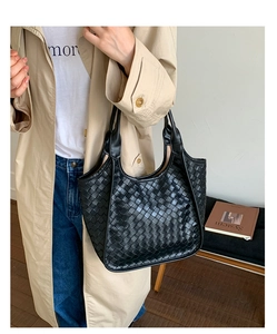 Dettaglio della trama intrecciata in pelle nera su una grande borsa tote minimalista con manici