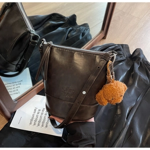 Close-up of deep brown vintage bucket bag featuring embossed logo and teddy bear charm
