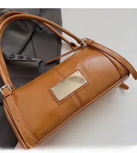 Close-up of brown PU leather baguette bag with metal plaque on a grey suit jacket