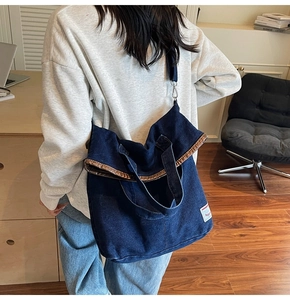 Detail of deep blue denim tote bag showing metal lining and wide crossbody strap on model