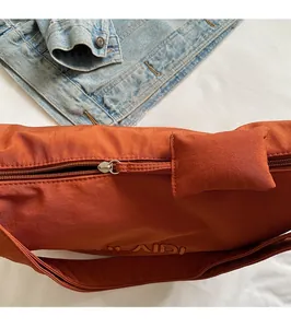 Detail of bright orange dumpling bag featuring a smooth metal zipper and embroidery