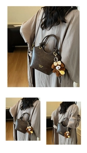 Detail einer braunen Vintage-Handtasche mit Goldlogo und süßem Bärenanhänger-Zubehör