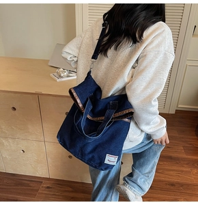 Detailed view of dark blue denim tote bag featuring brown metallic trim and long shoulder strap