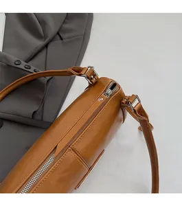Detail of smooth silver zipper and leather texture on a caramel brown cylinder crossbody bag