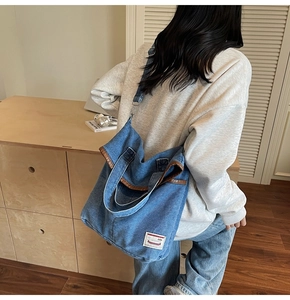 Blue denim tote bag with brown leather trim and shoulder strap worn by a female model