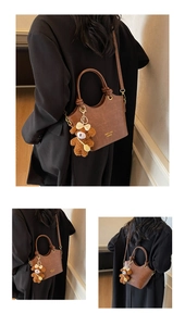 Detail einer braunen Vintage-Lederhandtasche mit Goldlogo und Plüschbär-Anhänger