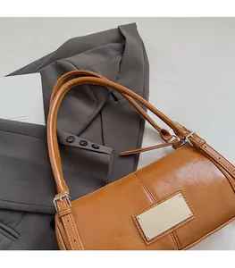 Detail of a brown leather shoulder bag with a silver metal plate on a grey blazer suit
