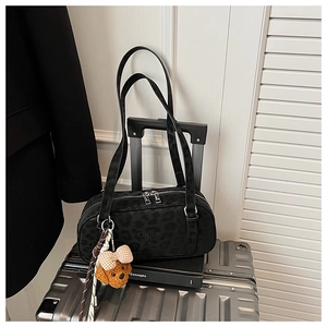 Detail of black leopard print suede handbag with silver zipper and plush dog charm accessory