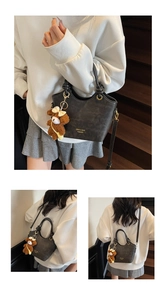 Detail der schwarzen Leder-Beuteltasche mit Goldlogo, Seilgriff und Bärenanhänger