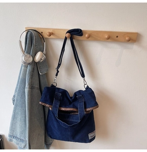 Detail of blue denim tote bag with adjustable strap and vintage label on a wall hook
