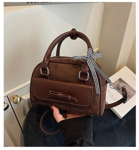 Détail du sac Boston en daim marron foncé avec bordure en cuir et nœud sur la poignée
