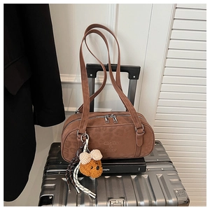Close-up of brown suede cylindrical shoulder bag with a cute plush bear charm on a suitcase