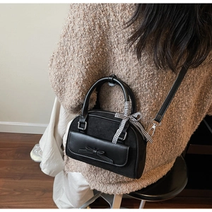 Détail du sac Boston noir avec ruban et nœud, porté par un mannequin dans un intérieur