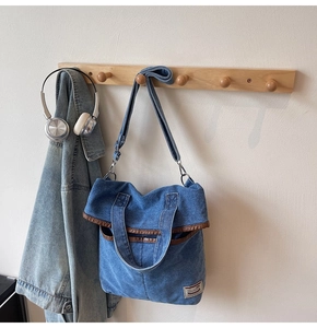 Detail of blue denim tote bag featuring brown leather trim and adjustable shoulder strap