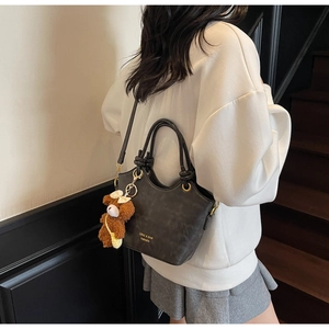 Schicke dunkelgraue Umhängetasche an Model mit Bärenanhänger und goldenem Logodetail